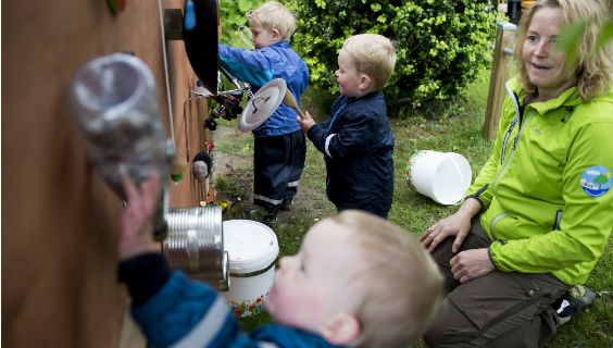 Naturdagplejer Lotte Damm Grevsen sidder foran en musikvæg, hun har lavet ud af genbrugsting. Tre børn er i gang med at afprøve den.